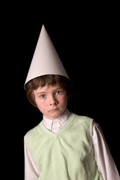 Sad young boy in a dunce cap over a black background
