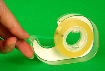 Female fingers pulling a piece of sticky tape from a dispenser