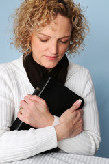 Obraz premium Young woman holding Bible and praying with eyes closed.