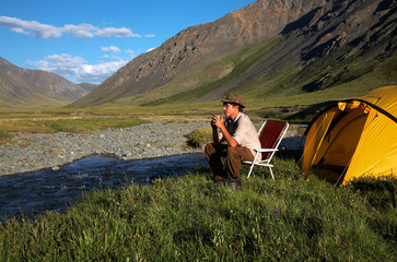 Fototapeta premium man is drinking at the camp in mountains near the stream