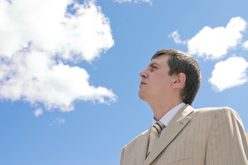 Young businessman looks upwards on a background of the blue sky