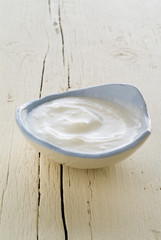 Yogurt in a small  pale blue bowl on a white wooden surface