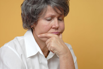 Very sad older woman in thought on yellow background.