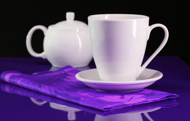 A coffee cup and teapot set on a blue/purple table table