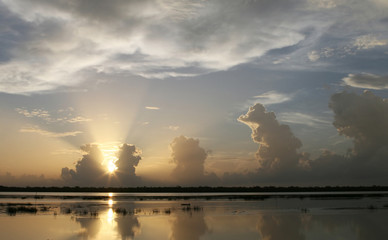 Naklejka na ściany i meble The sunrises up through puffs of clouds over a beautiful lake
