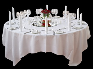 festlicher Esstisch mit weißer Tischdecke, Servietten und Blumenarrangement mit roten Rosen freigestellt auf schwarzem Hintergrund