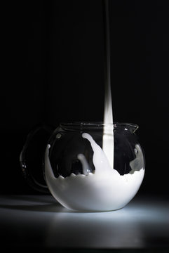 Milk is splashing in glass pot on black
