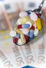 Bunte Tabletten auf Löffel und Geldscheine