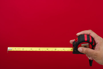 Tape measure in hand on red background with copy space