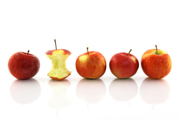 Apple core among whole apples, reflecting on white background.