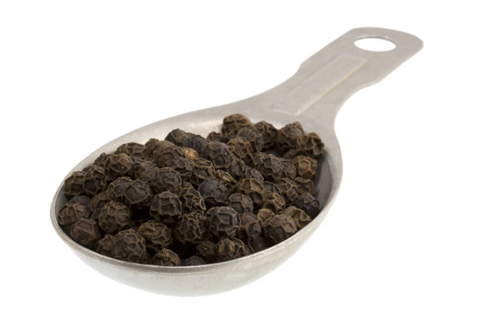 Measuring tablespoon of black peppercorns isolated on white