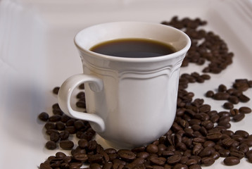Coffee in white cup with whole roasted beans on white plate