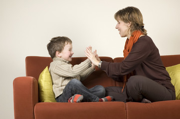 Mother and son are playing a clapping game on the couch.