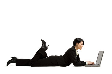 A businesswoman lying down on the floor typing on her laptop