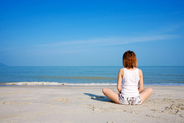 Fototapeta na wymiar woman meditate by the beach facing the sea with blue sky