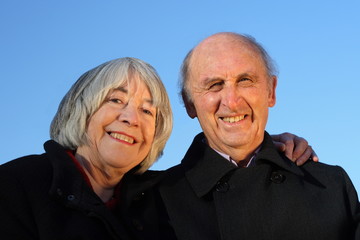 Senior couple embracing and smiling on a blue background.
