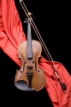 old violin with fiddlestick on folded scarlet silk diagonal