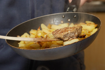 big cutlet on the woody handle and fried potatoes on pan