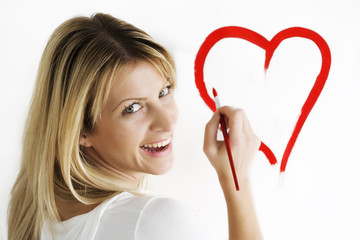 wsmiling young woman drawing heart-shape on white wall