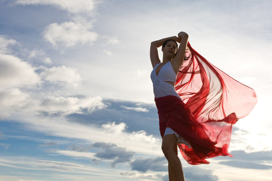 Frau mit rotem Tuch im Wind vor blauem Himmel