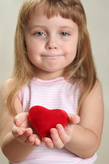 red heart in hands and slightly blurred child face ir background