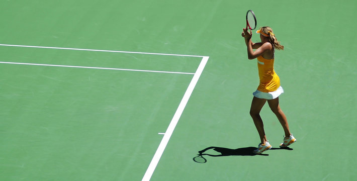 a girl in tennis action.  Yellow dress and green tennis field