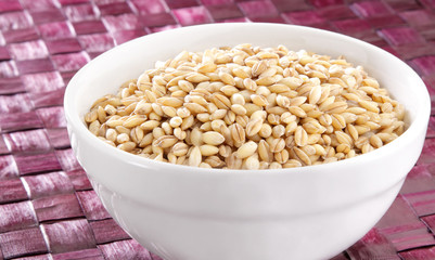 A bowl of organic barley on purple surface.