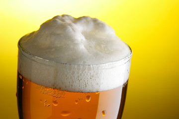 Mug of beer with froth close-up over yellow background