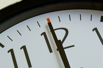 a black wall clock with a white face shows 12 o clock noon