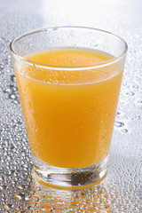 Orange juice on glass with drops on reflecting background
