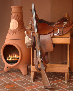 Saddle, rifle and kiva fireplace still life depicting New Mexico