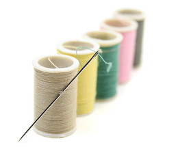 Several reels /spools of thread with a needle over white