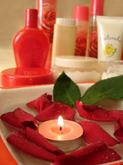 Obraz na płótnie Canvas red rose petals on water with candle and many bottles