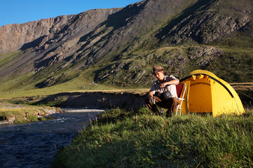 Fototapeta premium man is drinking at the camp in mountains near the stream