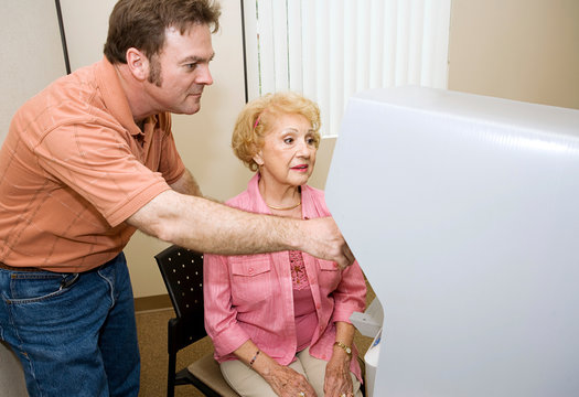 Young Male Poll Worker Assisting A Senior Woman With Voting