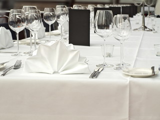 langer Esstisch mit weißer Tischdecke, gefalteten Servietten, Besteck, Brottellern und Weingläsern