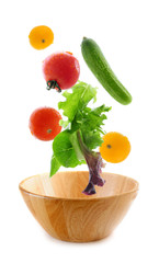 Assorted fresh vegetables falling into a wooden salad bowl 