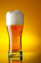 Poster Glass of beer close-up with froth over yellow background © Roman Sigaev