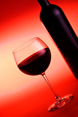 Wine bottle and wine glass against red background