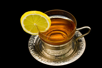 Transparent cup with tea and a lemon on a silver dish