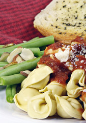 Tortellini with sauce and green beans and bread.
