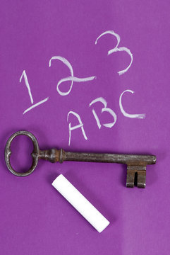 An old key sits on top of a childs chaulk board. 