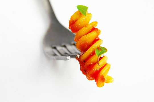 Closeup of rotini pasta on a fork, on white