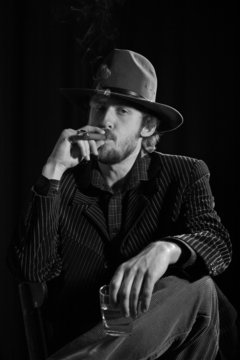 A monochrome image of a bearded man with cigar
