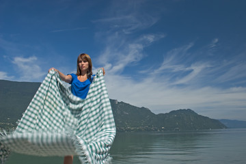 Fototapeta premium Woman extending a tablecloth for a picnic at the edge of a lake