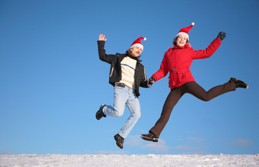 couple jump on snow in santa claus hats