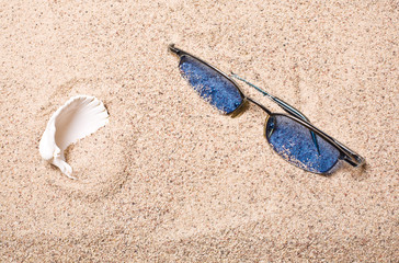 Fototapeta na wymiar Blue sun glasses and sheashell at sand close-up. 
