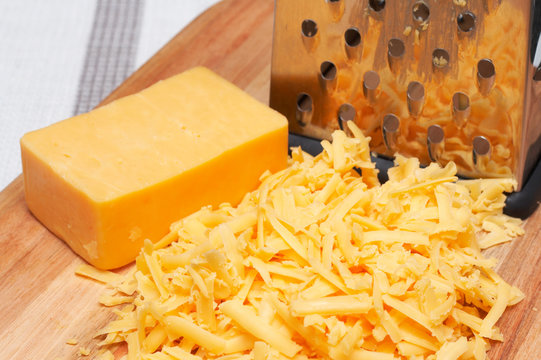 Grated cheddar cheese on wooden board with grater 