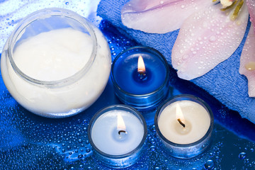 Obraz na płótnie Canvas spa essentials, cream, candles with flower on blue background