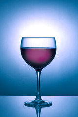 Glass of red wine silhouetted against a blue spotlight